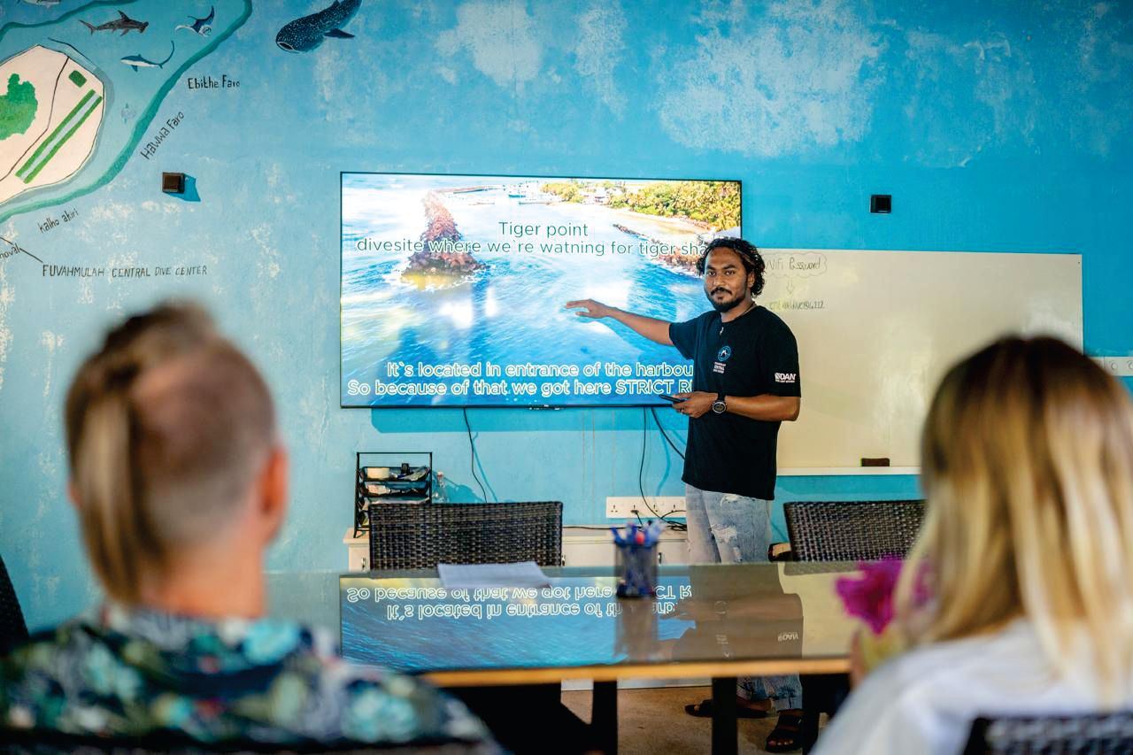 A dive guide briefing divers on the tiger shark site at the dive centre